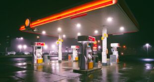 A brightly lit gas station on a rainy night with wet reflections on the ground.