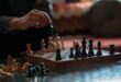 An intense chess match highlighting strategy between a pair of hands and chess pieces on a board.