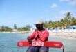 A lifeguard in red uniform sits at a tropical beach ready to ensure safety.