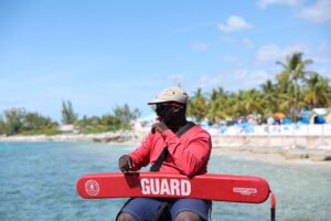 A lifeguard in red uniform sits at a tropical beach ready to ensure safety.