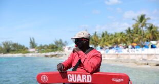 A lifeguard in red uniform sits at a tropical beach ready to ensure safety.