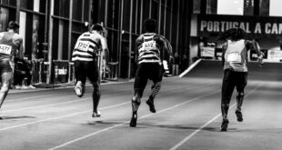 Back view of athletes sprinting on an indoor track, captured in grayscale.