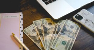 A workspace setup with dollar bills, notepad, and laptop on a wooden desk.