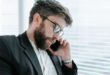 A bearded businessman in a formal suit engaged in a phone call indoors.