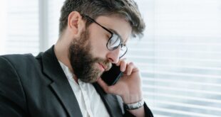 A bearded businessman in a formal suit engaged in a phone call indoors.