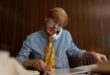 Red-haired businessman in glasses multitasking at his desk using a telephone and working on documents.