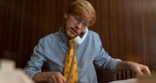 Red-haired businessman in glasses multitasking at his desk using a telephone and working on documents.